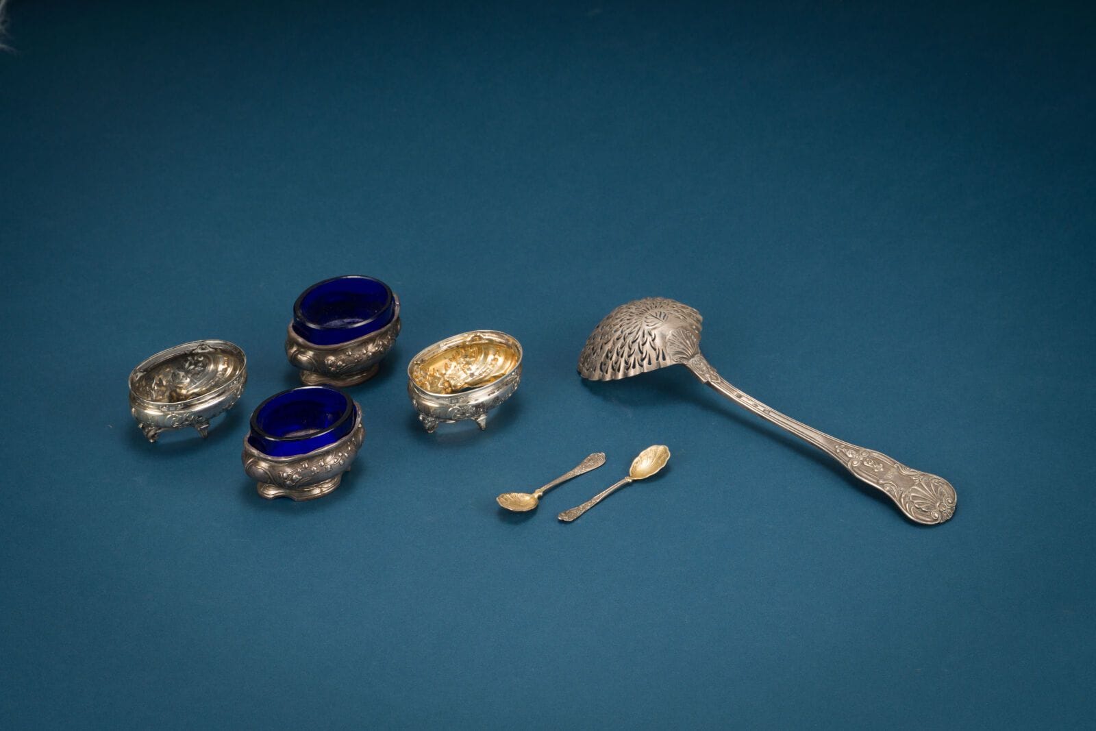 950/1000 silver sprinkling spoon, with a leaf and shell design.
Included are two pairs of 950/1000 silver salt cellars—one with a blue glass interior and the other without glass—and two 950/1000 silver salt spoons.
Total net weight: 204 g.
