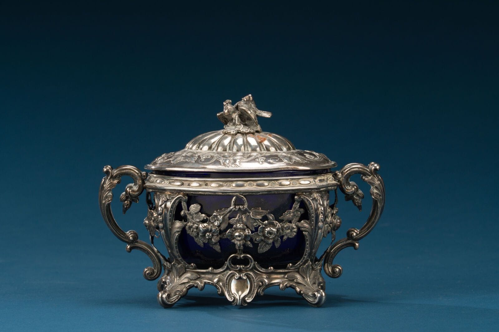 Silver sugar bowl with foliage decoration, bird-shaped handles, and a blue glass interior, 19th century.
15 x 19 x 11 cm.
Weight: 161 g.
