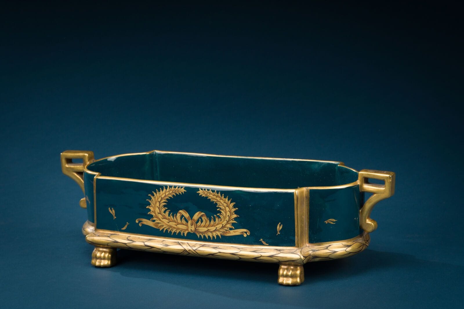 TOURS 
Porcelain planter decorated with gold-painted toruses and laurel wreaths on a blue background.
Manufactured by Jaget and Pinon.
Wear on the gilding. 
Height: 13 cm; Length: 44 cm.