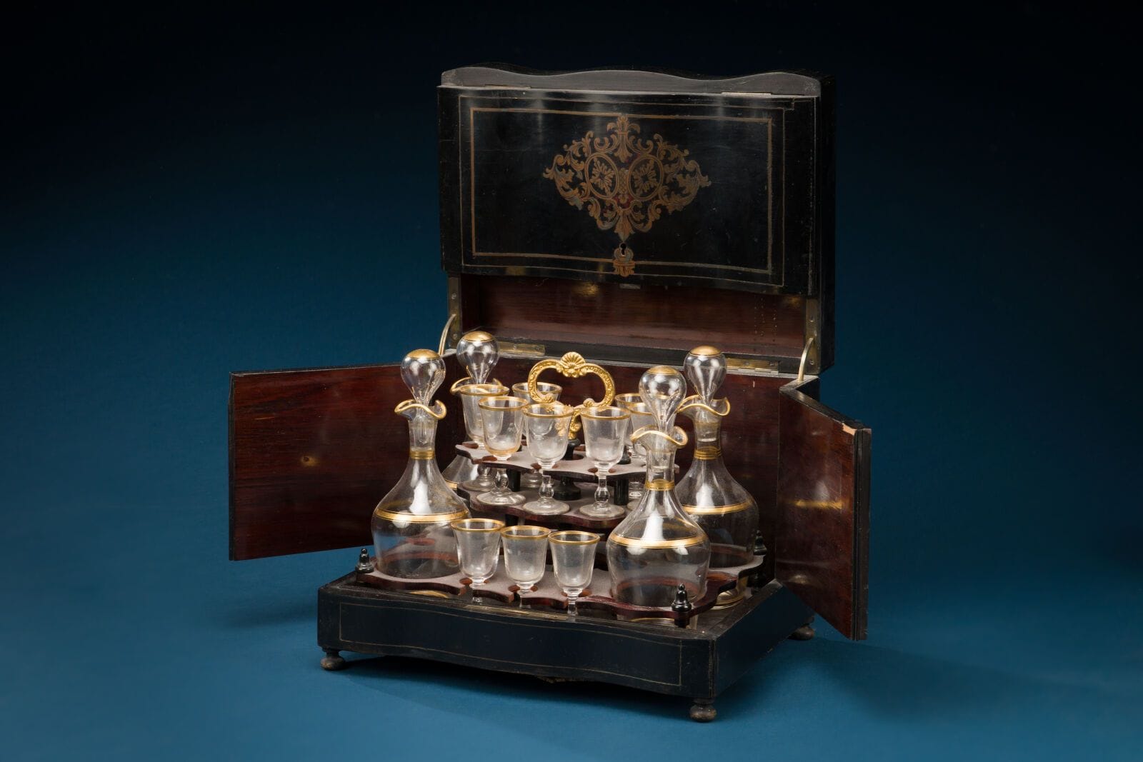 Liqueur set made of blackened wood with copper trim and cartouche decoration, including: 
- four decanters,
- ten glasses.
Napoleon III period
Dimensions (closed): 26 x 32 x 23.5 cm. 
(some glasses are missing)