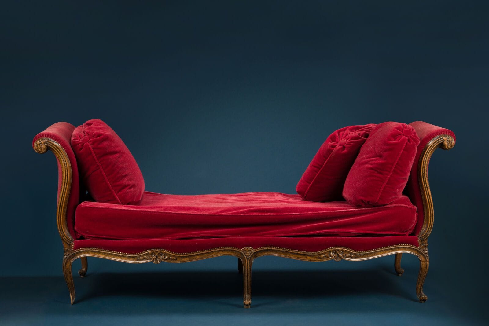 Natural wood sofa carved with foliage and small flowers, sloping backrest, curved legs,
Louis XV style, upholstered in red velvet. 
H.: 90 cm; W.: 220 cm; D.: 80 cm.
