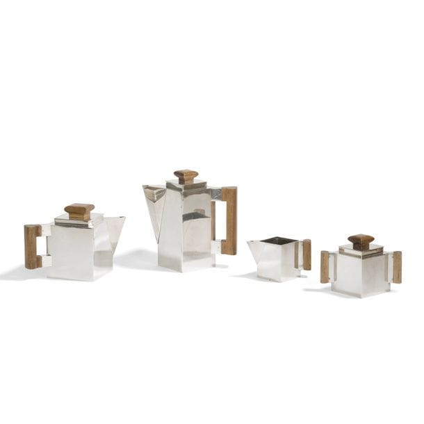 TRAVAIL MODERNISTE 
Service à thé et café en métal argenté composé d'un verseur à thé, d'un autre à café, d'un pot à lait et d'un sucrier. Le corps des pièces de section carrée. Prises et anses en bois. État d'usage, petit enfoncement à la base du verseur à thé et infimes chocs à la base du pot à lait. Chaque pièce porte le poinçon de Maître orfèvre.