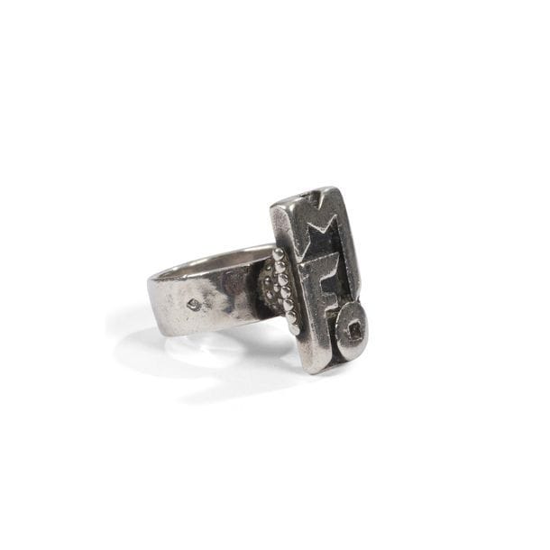JEAN DESPRÉS (1889-1980) 
Bague moderniste en argent. La plateforme rectangulaire encadrée de deux rangées de sphères présente un motif monogramme et repose sur un triple rang perlé formant un cylindre et accueilli par un anneau martelé. Signée J. DESPRÈS à la pointe à l'intérieur de l'anneau et porte les poinçons de Maître Orfèvre et de garantie sur l'extérieur de l'anneau. Poids : 14 g