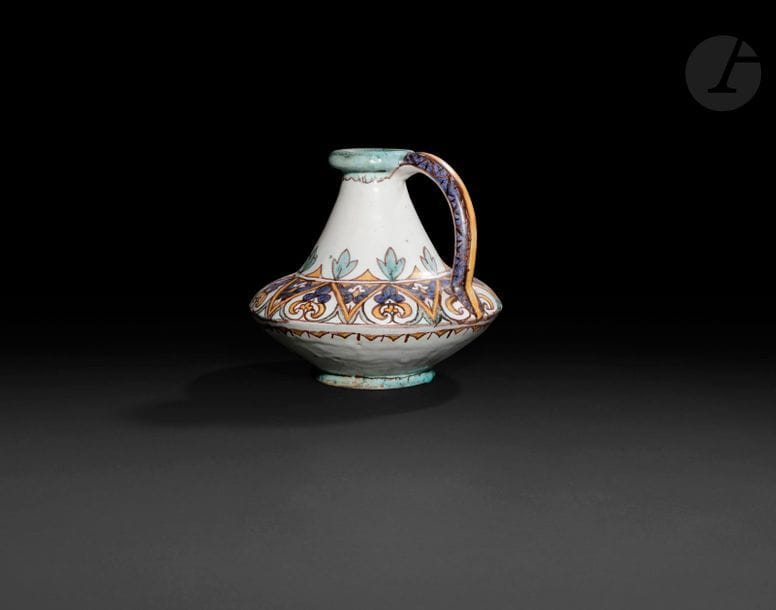 Vase toupie, Tunisie, Nabeul, XXe siècle 
Sur petit pied circulaire, à panse carénée, col tronconique et lèvre renflée, doté d’une anse latérale. Faïence à décor polychrome d’une frise de chevrons garnis de palmettes. Nom de l’atelier artisan en arabe et cachet estampé sous la base. 
Hauteur : 21 cm 
État : une entaille sur la partie inférieure de la panse. 

A polychrome pottery vase, Tunisia, 20th century 