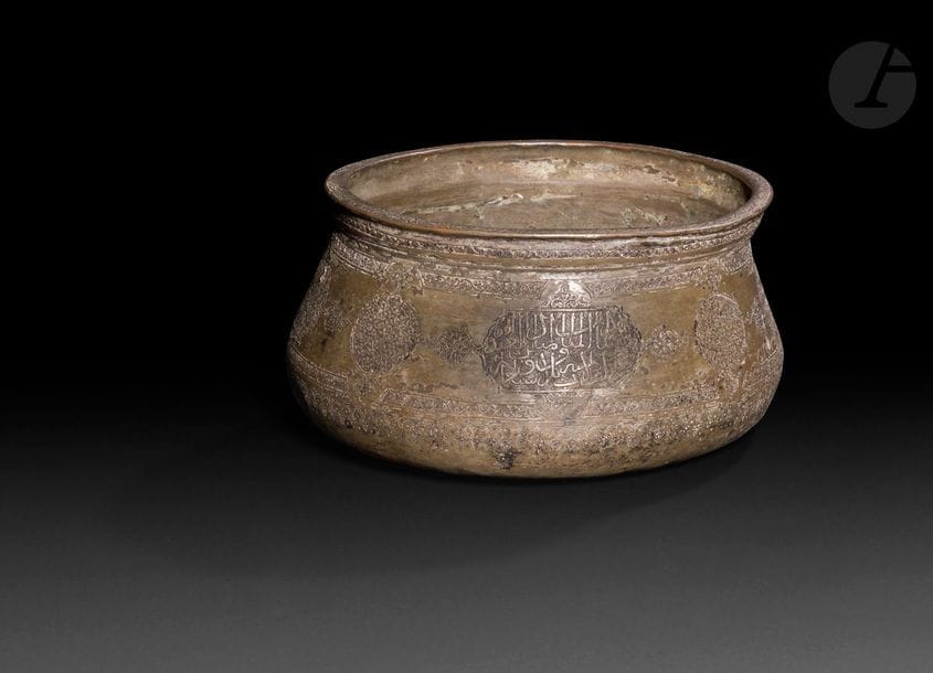 Bassin en cuivre étamé, Iran, fin XVe siècle 
Panse tronconique à décor gravé de médaillons circulaires et cartouches à appendices fleuronnés et décor floral, géométrique ou d’inscriptions en arabe. Une inscription religieuse en arabe cursif courant sur la lèvre. 
Hauteur : 10 cm ; diamètre : 18,5 cm 
État : chocs, fissure.

A copper bassin, Iran, late 15th century