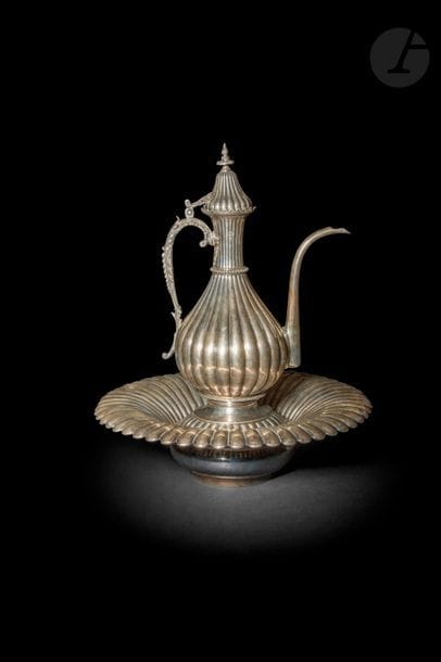 Aiguière et son bassin porte-savon en argent, Empire ottoman, Égypte, fin XIXe - début XXe siècle
Très belle aiguière ibrik à panse piriforme munie d’une anse foliacée et d’un couvercle surmonté d’une prise en forme de fleuron. Panse godronnée, ceinte d’un anneau perlé au col. Le porte-savon à godrons est muni d’une grille à décor rayonnant ajouré et porte la couronne du khédive d’Égypte ‘Abbas Hilmi gravée à l’épaule. Le bassin évasé est également godronné. Porte une tughra difficilement lisible et le poinçon sah.
Hauteur aiguière : 36 cm ; diamètre bassin : 40 cm
Poids : 3564 g

A silver ewer (ibrik) and basin, Ottoman Egypt, late 19th - early 20th century

 Il est difficile de lire le nom de la tughra du sultan Abdulhamid II (1876-1909). Le khédive ‘Abbas Hilmi était vice-roi d’Égypte sous le sultan ottoman entre 1892 et 1914, date à laquelle il fut déposé par les Britanniques.