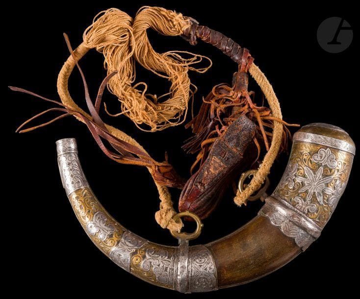 Poire à poudre en corne à monture en métal, Maroc, fin XIXe siècle
Corne à garnitures en métal et laiton, ciselées de motifs géométriques, à anneaux de suspension et cordons agrémentés d’un étui en cuir.
Longueur : 31 cm

A horn powder flask, Morocco, late 19th century