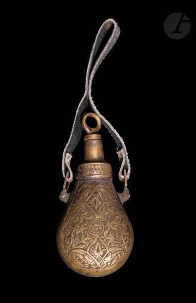 Poire à poudre en alliage cuivreux, Proche-Orient, portant la date de 1130 H /1717 
A décor gravé de rinceaux végétaux intégrant des fleurons et des palmettes sur fond de hachures. Sur une face, médaillon à inscriptions donnant la date de 1130 H / 1717. Bouchon à anneau se vissant. Lanière en cuir accrochée par deux anneaux mobiles. 
Hauteur : 13 cm ; avec lanière : 22 cm 
État : usure du cuir de la lanière. 

A brass powder flask engraved Near East with the date of AH 1130 / 1717