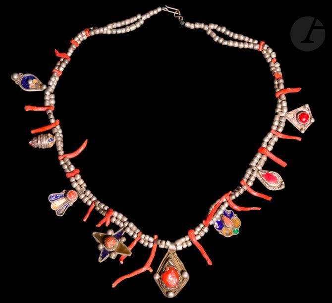 Deux colliers à pendeloques, azrar, Algérie, Grande Kabylie, première moitié du XXe siècle 
A double brins de perles de métal argenté scandés de corail, pour l’un en perles, pour l’autre, en brins et garnis de pendeloques en métal argenté émaillé polychrome, certaines serties de corail. 
Longueur : 44,5 cm et 46 cm ; poids brut : 192 g
État : sauts d’émail, corrosion.

Two necklaces with pendants, Algeria, Great Kabylia, 1st half of the 20th century 