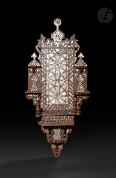 Porte-turban, kavukluk, Proche-Orient, début XXe siècle 
En bois incrusté de nacre et de filets d’étain à décor géométrique, floral, d’un croissant de lune embrassant une étoile dans la partie supérieure et d’une paire de vases à double anse de part et d’autre. Étagère principale mobile à charnière et présence de cinq petites étagères secondaires. 
Hauteur : 79 cm ; largeur max : 37 cm 
État : usures et manques.

A turban stand, kavukluk, Near East, early 20th century