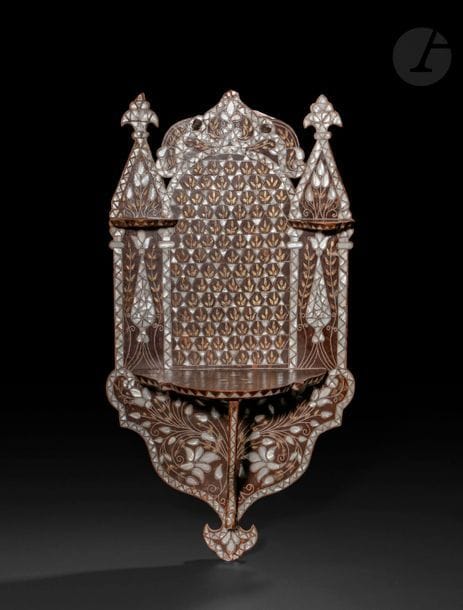Porte-turban, kavukluk, Proche-Orient, début XXe siècle 
En bois incrusté de nacre, de plaquettes d’alliage cuivreux et de filets d’étain à décor floral d’une résille de bouquets sous une arcature sur le champ principal, d’une paire de cyprès stylisés de part et d’autre et d’une gerbe florale sous l’étagère principale à cheville en volute. 
Hauteur : 74 cm ; largeur max. : 39,5 cm 
État : usures et manques.

A turban stand, kavukluk, Near East, early 20th century 
