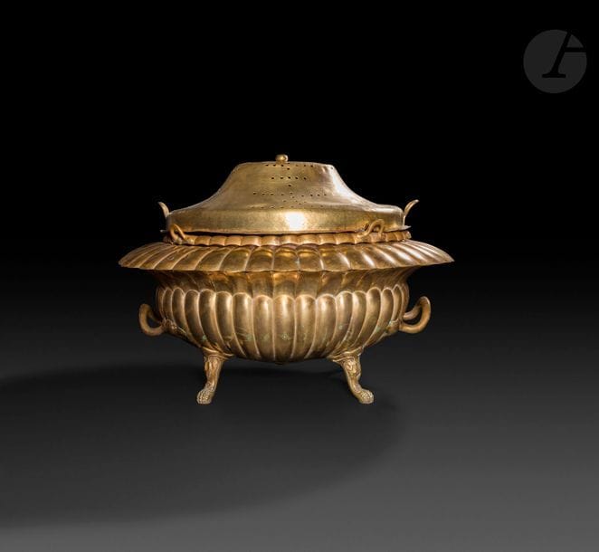 Brasero ottoman en laiton, Turquie, XIXe siècle 
Brasero à base godronnée reposant sur quatre pieds en pattes de lion et munie de deux poignées, cuve à braises amovible de forme ovale et dotée de quatre anses rivetées, couvercle convexe et ajouré à élément de préhension en boule. 
76 x 65 x 48 cm 
État : couvercle cabossé et fissuré, cuve rouillée. 

An Ottoman brass brasero, 19th century 