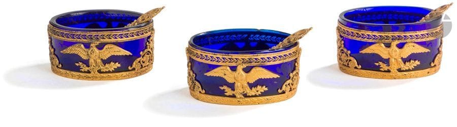 Trois salières en suite 
en métal doré, leur intérieur en verre bleu et leurs pelles à sel
Modèle d’inspiration Empire figurant Jupiter sous la forme d’un aigle les ailes déployées. 
