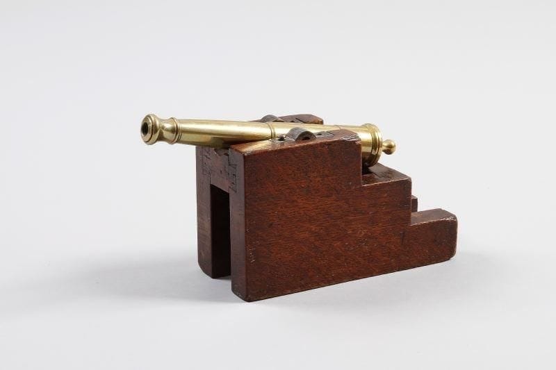 Maquette de canon de marine. Fût en bronze à bourrelet à la bouche, à quatre anneaux de renfort et deux tourillons. Monté sur un affût en chêne ciré. Long. canon: 22 cm. Long. totale: 25 cm. B.E. Fin du XIXè siècle.