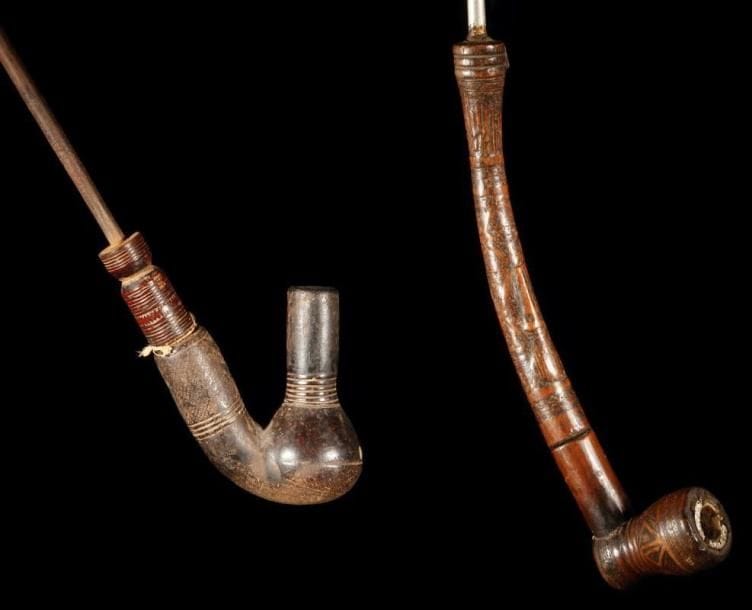 Lot de 2 pipes KUBA (R.D. Congo). L'une arquée en bois à patine brune, décorée de motifs géométriques ayant une signification symbolique. L'autre à fourneau en terre cuite finement décorée.. Longueurs:16 cm et 36 cm.