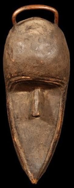 Masque TOMA (Guinée). «Masque» sans yeux et sans bouche, au menton très allongé, pointu, scarifications entourant le visage. Poignée de cuivre sur le haut du crâne. L'intérieur du masque est rempli de matières sacrificielles ce qui laisse à penser que ce masque non porté servait de reliquaire.. Hauteur:32 cm.