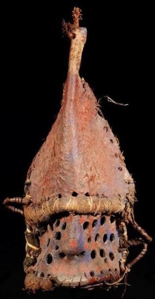 Masque IGBO (Nigéria). Très rare masque en cuir, formé de deux pièces cousues entre elles par de la fibre, la partie inférieure terminée par une barbe et trouée à l'emporte pièce de multiples trous. La partie supérieure en heaume. Ancienne patine brun rouge rehaussée de pigments rouges et bleus.. Hauteur:30 cm.