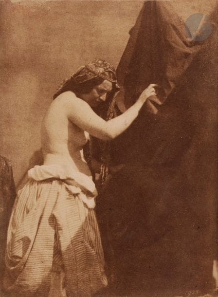 Julien Vallou de Villeneuve (1795-1866).
Étude de lumière (nu féminin au drapé), c. 1852-1853.
Épreuve sur papier salé-albuminé, d’après négatif papier, contrecollée sur carton souple. Numéro de négatif « 1923 » en bas à droite. Monogramme Vallou de Villeneuve et numéro de négatif reporté à la mine de plomb sur le montage en bas.
16,6 x 12,3 cm

 D’abord peintre et lithographe, e?le?ve entre autres de Franc?ois-Alexandre Pernot et de Jean-Baptiste Isabey, Vallou de Villeneuve de?bute la photographie a? la toute fin des anne?es 1840. Ses anne?es de formation sont tre?s peu documente?es. Il est probablement proche d’Humbert de Molard et be?ne?ficie des travaux de ce dernier sur le ne?gatif papier. On sait en revanche qu’il est membre de la Socie?te? He?liographique de?s 1851. Largement nourri de re?fe?rences picturales, ses nus soigneusement mis en sce?ne constituent e?galement des e?tudes d’apre?s nature pre?cieuses pour un peintre en que?te du re?alisme des postures et des chaires comme Gustave Courbet. (cf. Dominique de Font-Re?aulx, Laurence Des Cars et alii, Gustave Courbet, Paris, RMN, 2007). 