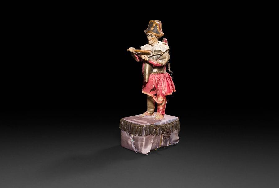 Personnage en carton bouilli figurant un polichinelle, revêtu de vêtements en soie, socle d’automate de marque LAMBERT et une clé ajourée des lettres LB. Mécanisme à revoir (ne fonctionne pas).
H : 48 cm