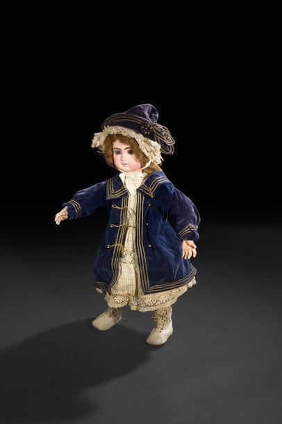 Bébé JUMEAU, tête en porcelaine marquée en creux : Tête JUMEAU Bté S.G.D.G, T.10, (reste l’ouverture au dos de la tête pour mécanisme), yeux fixes bleus, bouche fermée, oreilles percées, perruque châtain. Corps articulé en bois et composition, robe en guipure sur fond bleu et bonnet, on y joint son manteau et son chapeau en velours bleu marine.
H : 60 cm