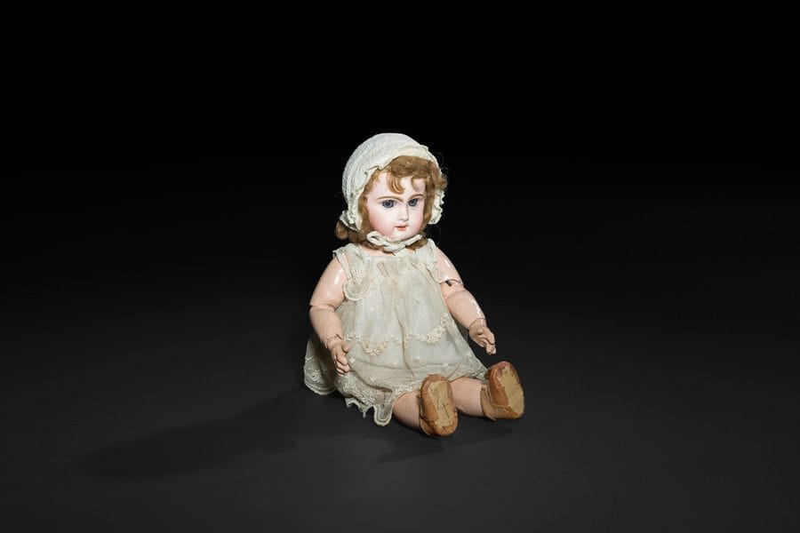Bébé JUMEAU, tête en porcelaine marquée au tampon rouge : Déposé Tête JUMEAU, T.7, yeux mobiles bleus, bouche ouverte sur une rangée de dents, oreilles percées, perruque blond foncé. Corps articulé en bois et composition, reste de tampon bleu : Bébé JUMEAU Bté S.G.D.G - Déposé, robe en tulle brodé et bonnet blanc.
H : 45 cm