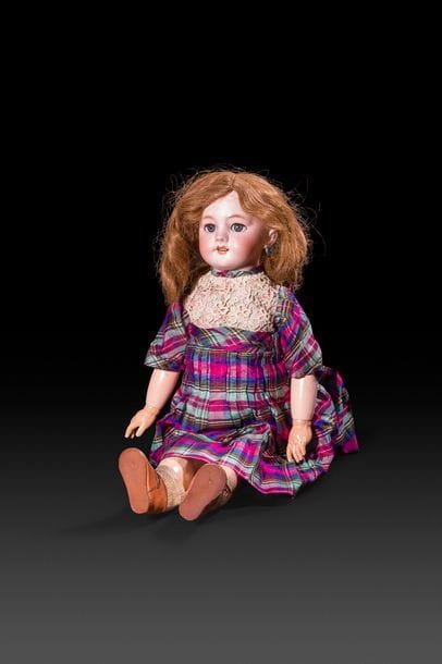Poupée tête en porcelaine, marquée en creux : DEP, yeux mobiles bleus, bouche ouverte sur une rangée de dents, oreilles percées, perruque châtain clair. Corps en composition, jambes raides (à système marcheur) robe en soie écossaise à plastron en crochet.
H : 58 cm