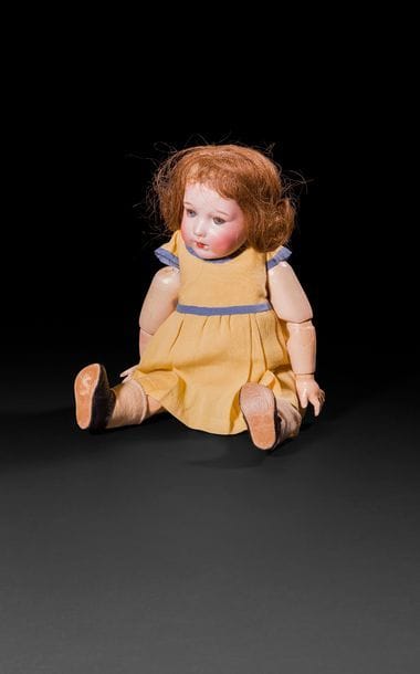 Bébé Caractère, tête en porcelaine marquée en creux : SFBJ 251, T.6, yeux mobiles bleus, bouche ouverte laissant apparaître la langue et deux dents, perruque rousse. Corps articulé en bois et composition. Robe jaune à ruban bleu.
H : 40 cm