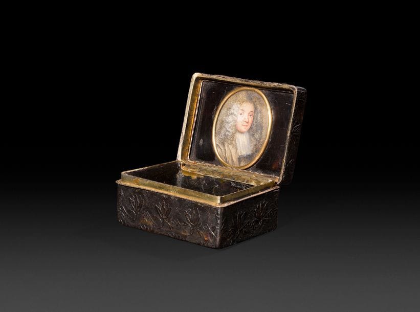 PARIS, 1750-1756
Tabatière en écaille et monture en vermeil de forme rectangulaire ouvrant à charnière, sculptée de rangs de fleurs dans des losanges toutes faces, elle découvre à l’intérieur du couvercle une miniature représentant un gentilhomme du XVIIIe siècle de trois quarts dans un ovale.
(Infimes trous de mites).
L : 8,3 cm - largeur : 6 cm - H : 4 cm