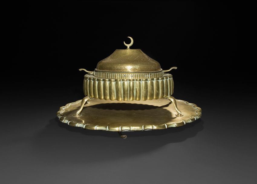 Brasero ottoman en laiton, Turquie, fin XIXe siècle.
Brasero à base godronnée reposant sur quatre pieds, cuve à braises amovible flanquée de deux poignées coquille et couvercle convexe à décor de courbes ajourées et d’un croissant de lune au sommet. Accompagné de son plateau à roulette en laiton doré à découpe festonnée.
(Quelques rayures, coups, sauts de dorure).
63,5 x 45 x 47 cm