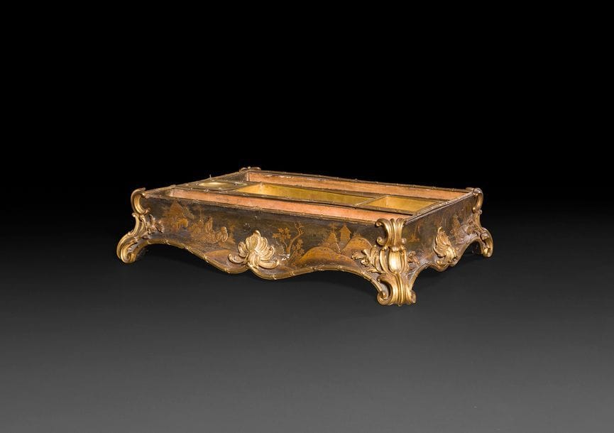 Grand encrier en laque du Japon et vernis parisien, la monture de bronze doré à chutes ajourées dans les angles, coquille stylisée et feuillages, avec deux grands compartiments (manques au vernis), plumier, encrier et sablier (manques).
Bronzes marqués du c couronné (1745-1749)
Époque Louis XV (accidents).
H : 9 cm, L : 28,5 cm, P : 37 cm

Bibliographie :
P. Hughes, The Wallace Collection catalogue of furniture, Londres, 1996, p. 320-322).
 L’encrier en laque du Japon très proche est aujourd’hui conservé à la Wallace Collection de Londres. Malgré quelques différences, les deux encriers peuvent être attribués au même atelier d’ébénisterie ; réalisés à la même époque, ils sont tous les deux marqués du C couronné. Un encrier semblable faisait partie de la collection Jacques Malatier à Paris (sa vente à Paris, étude Ader, le 10 octobre 2018, lot 235).
