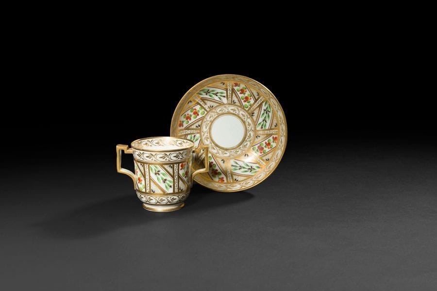 Derby
Tasse à deux anses et sa soucoupe en porcelaine de fleurs dans des galons sur fond or.
Marquées.
Fin du XVIIIe siècle. 
H : 8 cm, D : 15 cm
