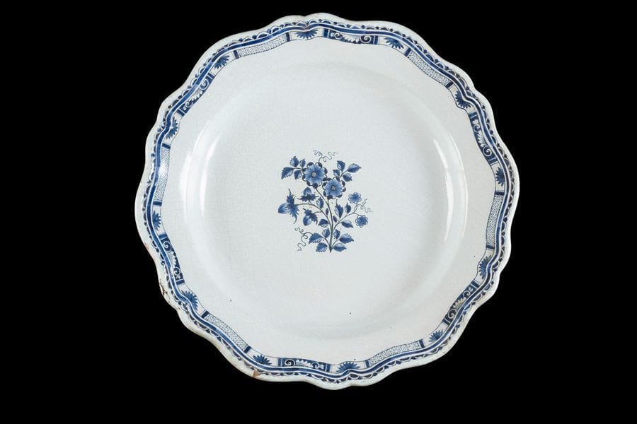 Rouen
Grand plat rond en faïence à bord contourné à décor en camaïeu bleu de fleurs au centre et d’un galon sur le bord.
XVIIIe siècle. 
D : 49 cm