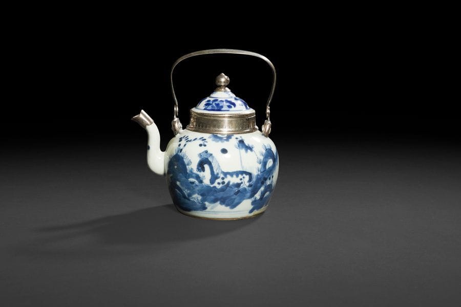 Théière et un couvercle en porcelaine à décor en bleu sous couverte de chevaux dans des paysages, fleurs sur le couvercle.
XVIIIe siècle. 
Monture et anse en argent européen.
(Accidents et restaurations).
H : 14 cm