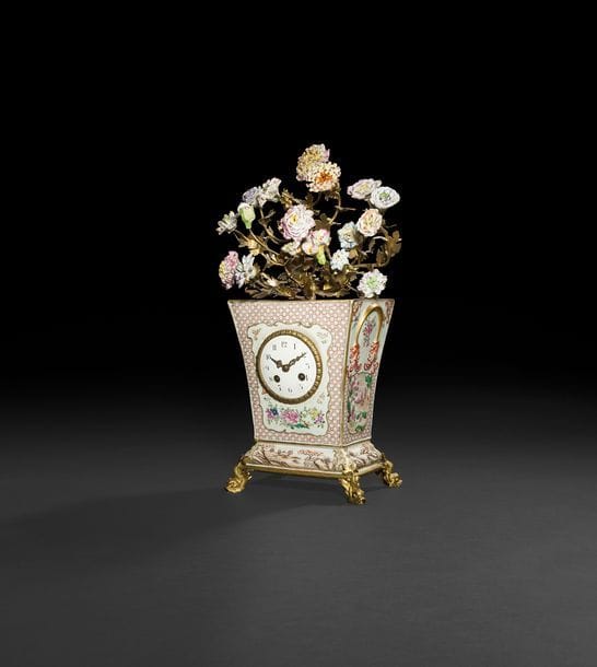 Pendule en porcelaine imitant la porcelaine de Chine à décor de branchages fleuris et paysages, reposant sur une base à figures de dauphins ; surmontée d’un bouquet de fleurs de porcelaine.
Fin du XIXe siècle (accidents).
H : 26 cm, L : 20 cm, P : 15 cm