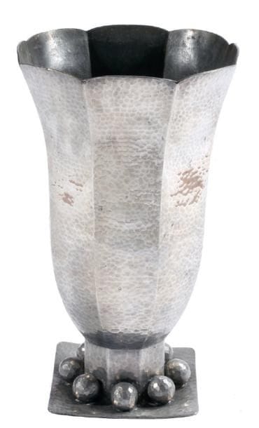 Jean DESPRES (1889-1980)
Important vase tulipe réalisé en dinanderie d'étain à surface entièrement martelée. Base à pans coupés, ornés de sphères facettées, reposant sur une terrasse de section carrée. Travail des années 30/40. Signé à la pointe à deux reprises sur et sous la terrasse. Hauteur: 34,5 cm. Provenance: Acquis directement auprès de l'artiste par la famille (avallonnaise) des actuels propriétaires