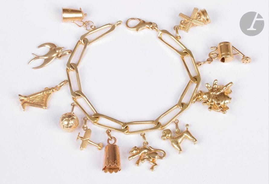 Bracelet en or 18K (750), orné de 11 charms en or jaune 18K en pampilles : un moulin à vent, un arrosoir, une abeille, un caniche, un singe, une clochette, un avion, un ballon, une harpe, une hirondelle et une cafetière. Poids : 36,9 g