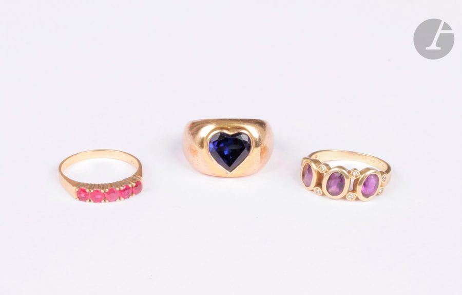 Lot de 2 bagues en or 18K (750), l'une sertie d'améthystes ovales scandées de petits diamants ronds, l'autre agrémentée de rubis synthétiques. Poids brut : 7,8 g (accident, on joint une bague en métal ornée d'une pâte de verre bleue cordiforme)