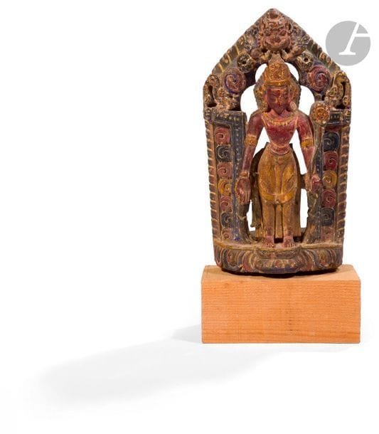 NéPAL - XVIIe / XVIIIe siècle
Groupe en bois sculpté à traces de polychromie, Padmasambhava debout devant une porte en forme de mandorle surmonté d’une tête de Kirtimukha, une tige de lotus se dressant de sa main gauche le long de son bras. 
H. 27 cm