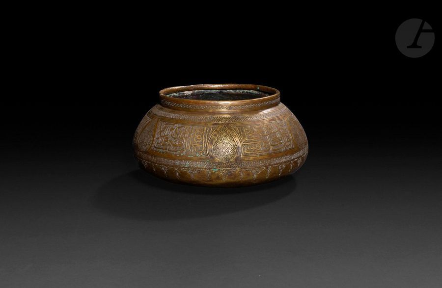 Bassin tâs, Proche-Orient, XIXe siècle
Bassin en laiton, à base bombée, panse renflée et lèvre droite, à décor gravé de cartouches à pseudo-calligraphie arabe séparés par des médaillons en amande meublés d’une résille géométrique. Plusieurs chiffres gravés sous la base.
Diamètre ouverture : 16 cm ; hauteur : 11 cm 
État : accidents, traces d’oxydation

A brass bassin, tâs, Near East, 19th century