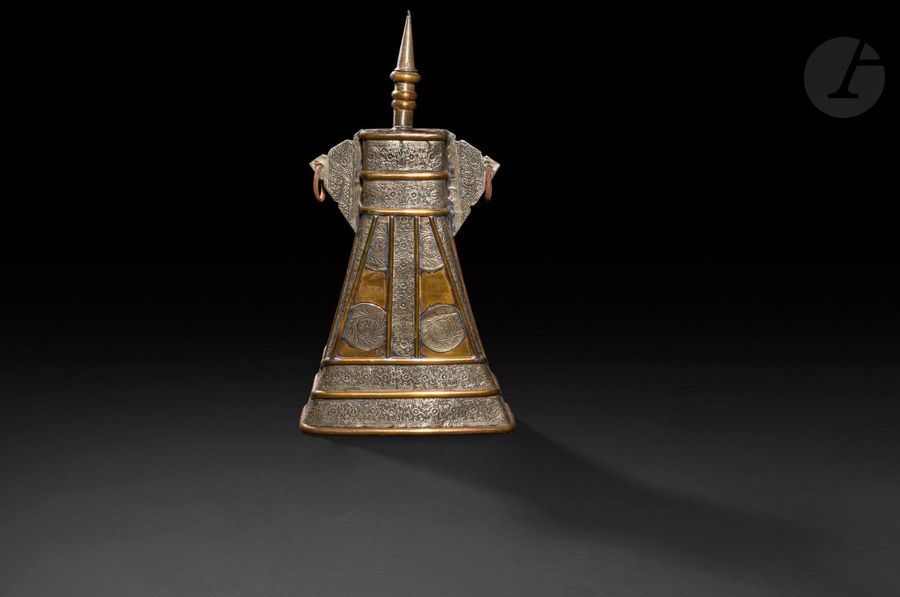 Grande boîte à poudre, Afrique du Nord, fin XIXe-début XXe siècle
En laiton à garnitures en métal argenté à décor floral moulé de rinceaux disposés en volutes. Corps tronconique à oreilles en khema, bouchon en forme de minaret. 
Hauteur : 54,5 cm
État : accidents, anneaux rouillés, bouchon instable.
On y joint deux poires à poudre, une petite de forme coudée, Proche-Orient, une seconde en forme de corne en alliage cuivreux à décor moulé, Maroc.

A large powder flask, North Africa, 19th-20th century