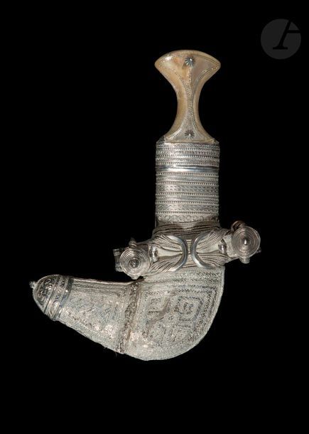 Poignard, jambiyya, Yémen ou Oman, début XXe siècle
A lame courbe à double tranchant et nervure médiane. Monture en corne ornée de clous en argent et de petites pastilles. Fourreau en argent à décor de compartiments à motifs géométriques ou lignes perlées. Sur le coude, anneaux et attaches de boucle tenus par des fils d’argent. Au revers, cuir uni vert.
Longueur : 29 cm ; poids brut : 150 g

A dagger jambyya, Yemen or Oman, early 20th century