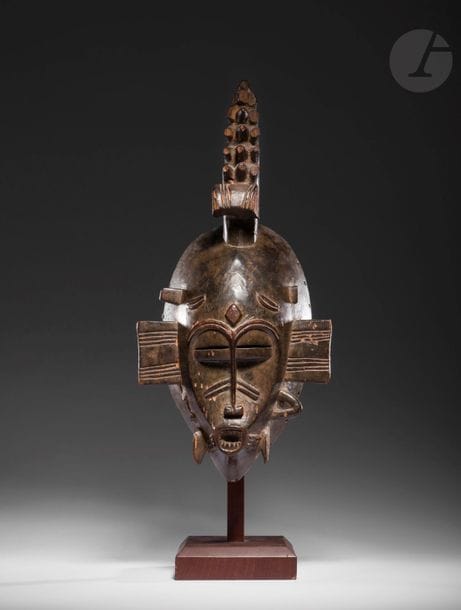 Un très beau et ancien masque Kpelie.
Ce masque de caractère féminin incarne la stabilité, le calme, l'équilibre et l'unité, mais aussi l'accomplissement féminin, donc la fertilité ; ces masques sont en grande majorité caractérisés notamment par une scarification au centre du front dont la symbolique était autrefois gardée secrète, et évoquait un rite d'initiation non moins secret, d'un grade supérieur, consistant à s'unir à la terre-mère, une étreinte qui scellait le mariage des initiés avec la société du Poro. 
Cet exemplaire ancien n'est pas sans rappeler avec sa bouche qui avance et montrant ses dents le fameux exemplaire de l'ancienne collection René Rasmussen auquel il manque aussi une grande partie de ses appendices.
Senoufo, Côte d'Ivoire
Bois, manques visibles des appendices (casses anciennes), très belle patine d'usage 
H. : 33,5 cm

Provenance : 
Ancienne collection Maurice Garin, acquis entre 1950 et 1955