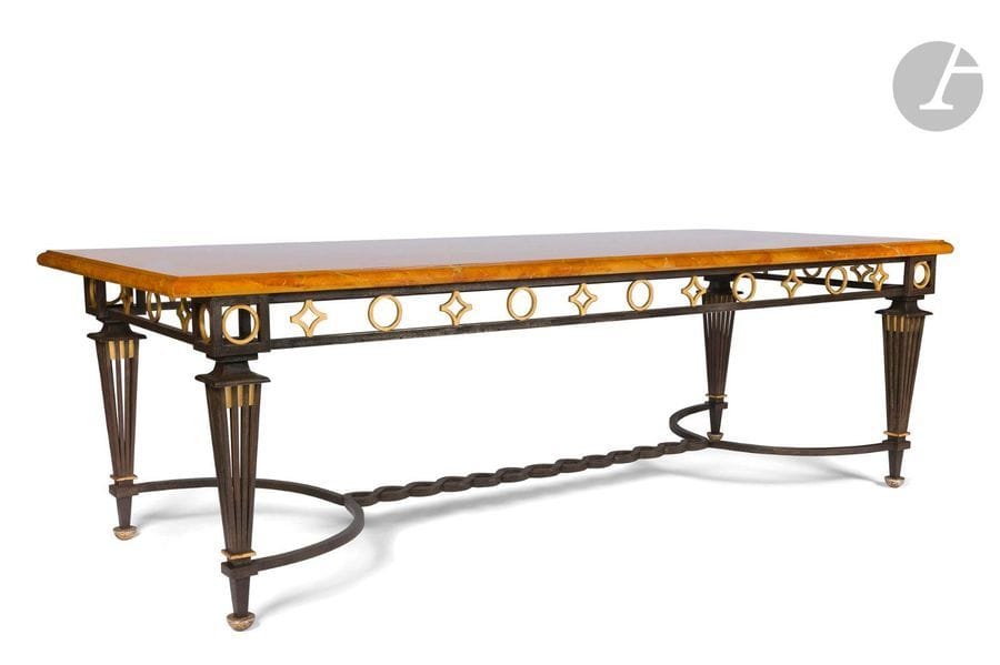 GILBERT POILLERAT (1902-1988
)Pieds fuseaux ajourés - Croix templières et cercles, le modèle
 présenté au 34e Salon des Artistes Décorateurs, Paris, 1948Rare

 et importante table de salle à manger néoclassique

 en fer forgé patiné ; les motifs ornementaux dorés.

 Les quatre pieds d'angle en gaine ajourée, chacun sommé d'une scotie et reposant sur un patin en demi-sphère renversée, sont réunis par une entretoise en

 accolade à l'arête centrale évoquant un tressage.

 La ceinture, également ajourée, reçoit des motifs titres et

 présente des dès d'angle aux décors de cercles. 

Le plateau rectangulaire, au pourtour mouluré façon bec de corbin, est exécuté en laque sur âme

 de bois à l'évocation d'une pierre marbrière. Vers 1950
.Hauteur : 77cm
 - Longueur:240cm - Largeur:105cmProvenance
:- M. Auguste Veuillet (1910-1980), coureur automobile, fondateur de Sonauto (1947), 1er importateur Porsche en France (engageant en 1951 la première voiture de la marque au 24 heures du Mans qui sera la gagnante de sa catégorie). Table acquise pour son importante propriété du
 domaine de La Chaurie (Sologne).

 - M. et Mme M. (Sologne). Œuvre acquise en 1981 lors de l'achat de la propriété de La Chaurie aux héritiers d'Auguste Veuillet suite à son décès l'

année précédente. Bibliographie
:- Mobilier et Décoration - Salon des Artistes Décorateurs - N°6 de juin 1948. Une table identique, recevant un plateau en marbre
, reproduit page 23

.- Art et Industrie - N°XVI année 1949. Une table identique, recevant un plateau en marqueterie de marbres, reproduit pages 34

 et 35

.- Ferronnerie d'aujourd'hui - Présentation et introduction de Gilbert Poillerat, Éditions d'Art Charles Moreau, Paris, vers 1946/48. Un modèle identique, légèrement plus petit et recevant un plateau de marbre, reproduit

 planche31.<
