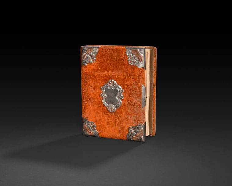 Album de photo à musique. Vers 1890.
Reliure à couverture de velours orange, ornée d’un écusson et de coins en étain sur le premier plat. Les feuillets intérieurs contiennent quelques anciennes photos de famille. Dans l’épaisseur du dernier plat de la reliure, protégé par une vitre un mouvement de musique type tabatière joue de la musique lors de l’ouverture du fermoir de l’album. 
450 x 270 mm