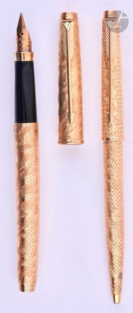 BOUCHERON
Parure stylo plume et stylo bille en or 18 carats tressé puis gravé avec un décor moiré. Réalisée sur une base de Parker 75. Plume or 18 carats, remplissage cartouche. Bille avec capuchon poussoir. Corps du plume légèrement tordu. Micro-rayures. 
Longueur du plume : 130 mm - Poids brut de la parure : 54 g
