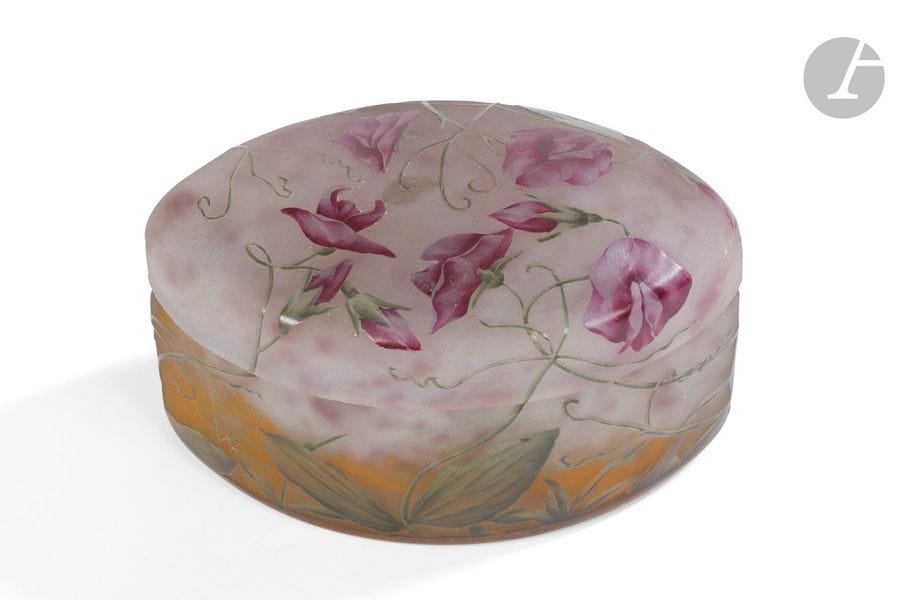 DAUM NANCY
Pois de senteur
Bonbonnière de forme navette. Épreuve en verre au décor dégagé à l’acide et émaillé polychrome sur fond marmoréen gris nuancé de rose et de mandarine à la base. Infimes égrenures sur la réception et sur le couvercle. Signé DAUM NANCY à la Croix de Lorraine, en réserve gravé en camée à l’acide. 8 x 13 x 8,5 cm 