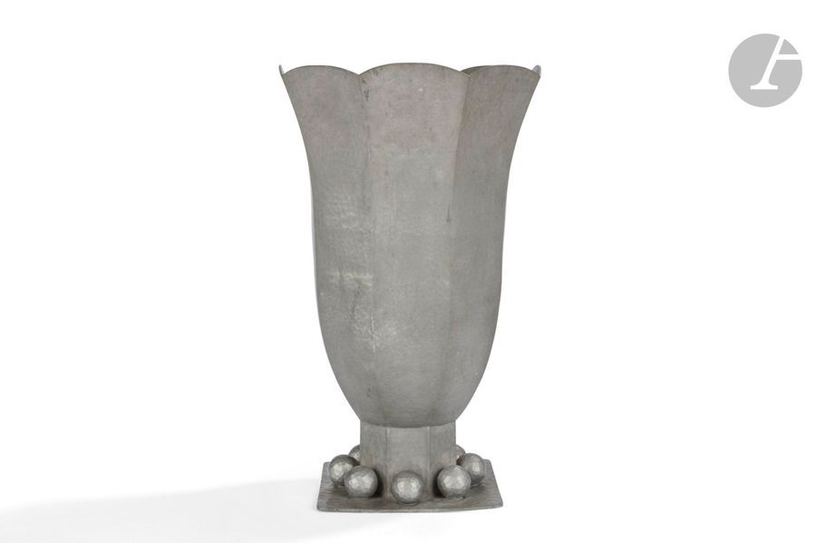 JEAN DESPRÉS (1889-1980)
Tulipe et sphères, pour M. Gaston Gaudaire, 1947
Haut vase cornet à facettes reposant sur une terrasse carrée. Épreuve en dinanderie d’étain montée au marteau et à surface entièrement martelée. Le corps du vase, terminé en découpe sur sa partie haute, est reçue pas une base octogonale accueillie par la terrasse enrichie de huit importantes sphères facettées. Signé 
J. DESPRÉS à la pointe sur la terrasse et inscrit : La Fédération des Sociétés Musicales de l’Yonne à Monsieur Gaston Gaudaire son Fondateur et Président 1907-1947, sous la base. H. 34,5 cm