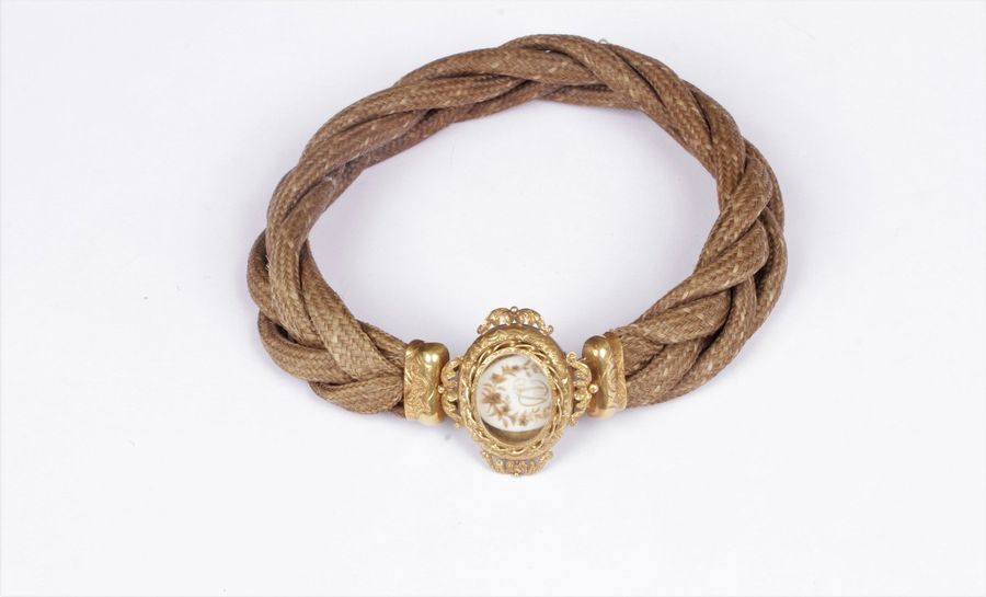 Chaîne en cheveux tressés, fermoir en or jaune 18K (750) ciselé, il recèle une miniature en cheveux appliqués dessinant le chiffre PD dans une couronne de fleurs. Longueur : 31 cm environ. Poids brut : 17,7 g