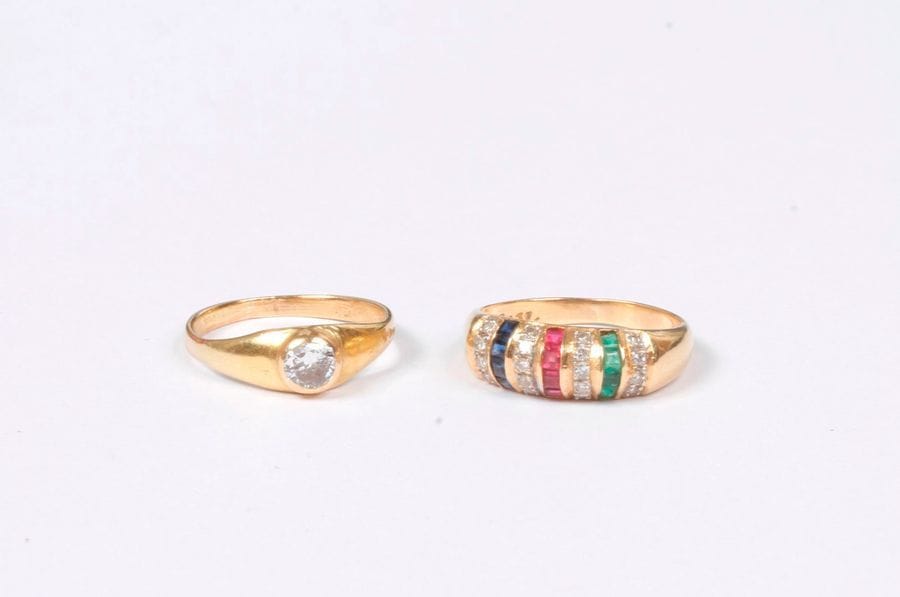 Lot de deux bagues en or 18K (750), l’une ornée d’un diamant rond de taille ancienne, l’autre agrémentée de diamants ronds entre des lignes de pierres vertes, rouges et bleues synthétiques. Poids brut : 5,8 g (accident)