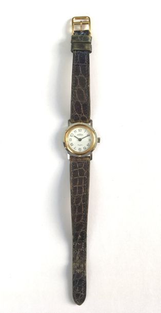 HERMèS. Vers 1990
N° 33768 Montre bracelet de femme en métal doré et acier, cadran blanc, index chiffres arabes formant les heures. Date par guichet à 3h, mouvement à quartz (pile à vérifier), bracelet cuir avec boucle ardillon en métal doré.